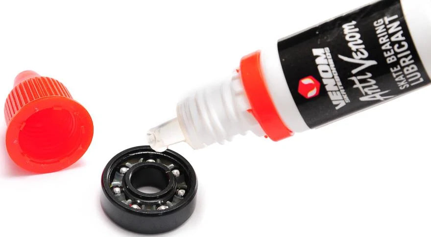 A Venom AntiVenom Bearing Lube 10ml bottle applying a drop of clear liquid into a black skateboard bearing.