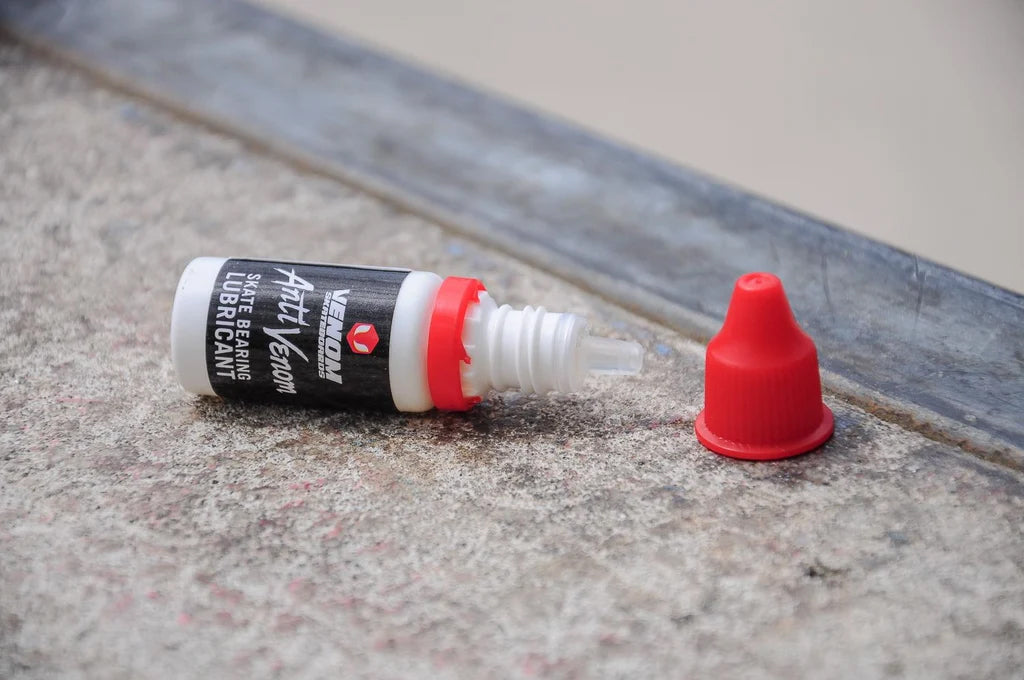Venom AntiVenom Bearing Lube 10ml bottle with its red cap removed, lying on a concrete surface.