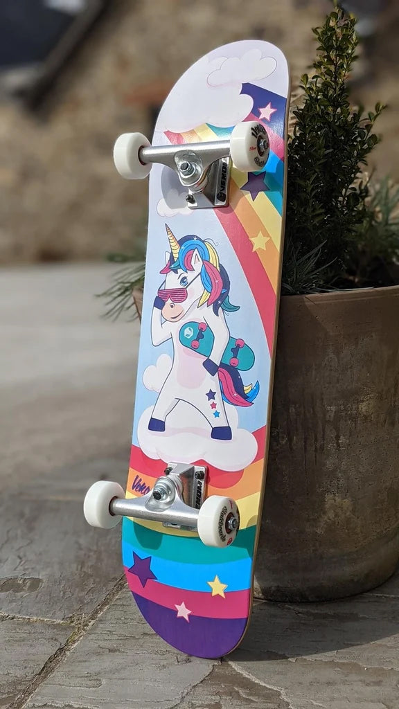 Venom Junior Unicorn Kids Complete Skateboard - 7.25″ x 29″ featuring a cartoon unicorn wearing sunglasses and carrying a smaller skateboard, set against a background of clouds, stars, and a rainbow.