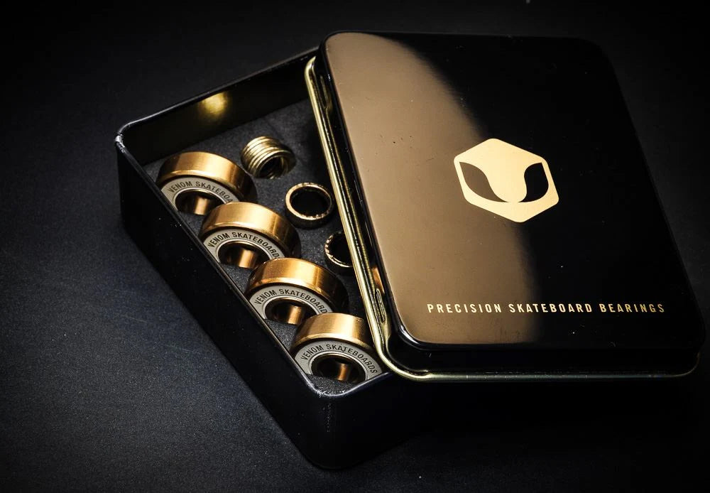 An open black tin case revealing eight gold-toned Venom Precision Gold Skateboard Bearings - 8 Pack arranged inside.