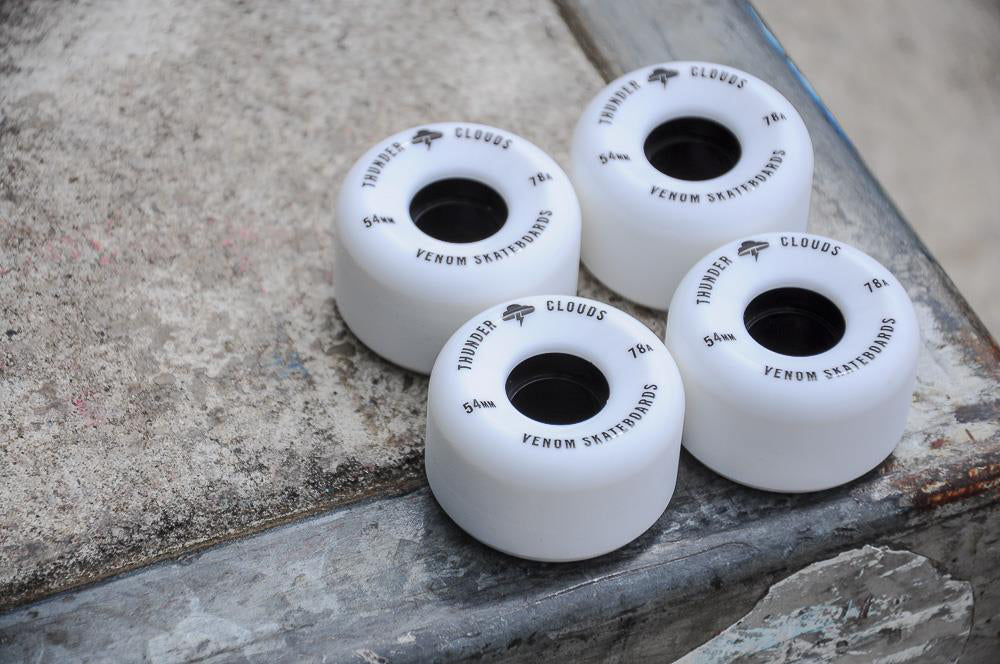 Four white Venom Thunder Clouds V2 54mm 78A Skateboard Wheels with black text arranged on a concrete surface.