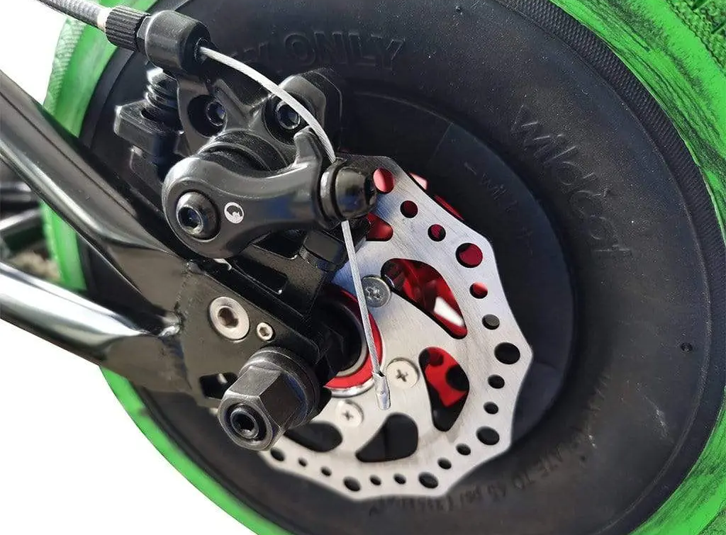 Close-up of the Wildcat 10" Mini BMX Rear Disc Brake showcases the detailed disc brake system and caliper on a black rim with a green tire. The silver brake rotor features red accents, highlighting Wildcat's quality engineering.