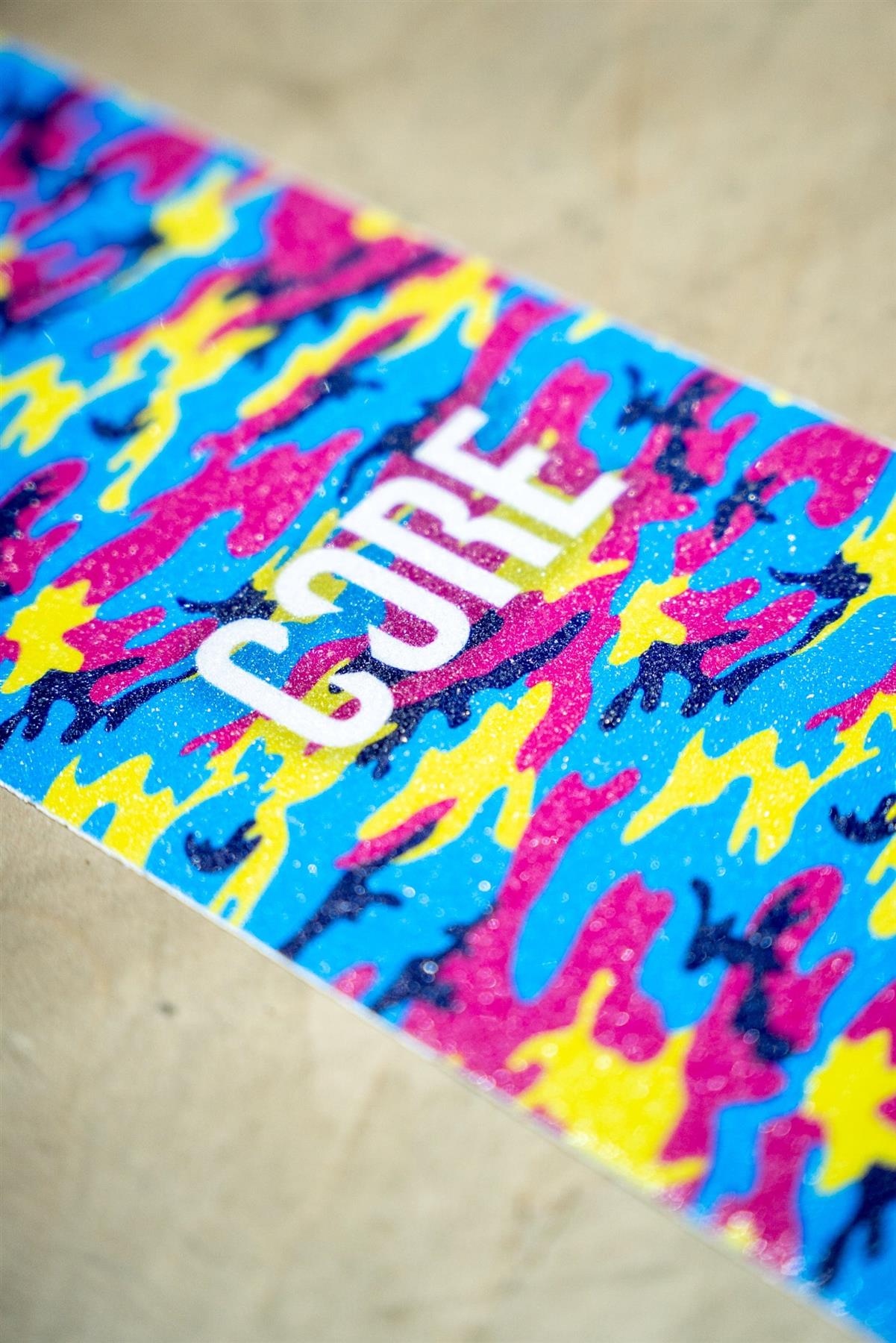 The CORE Stunt Scooter Griptape - Neon Camo by CORE features a vibrant blue, pink, and yellow camo design with "CURE" in bold white letters—making it a stylish upgrade for your stunt scooter.