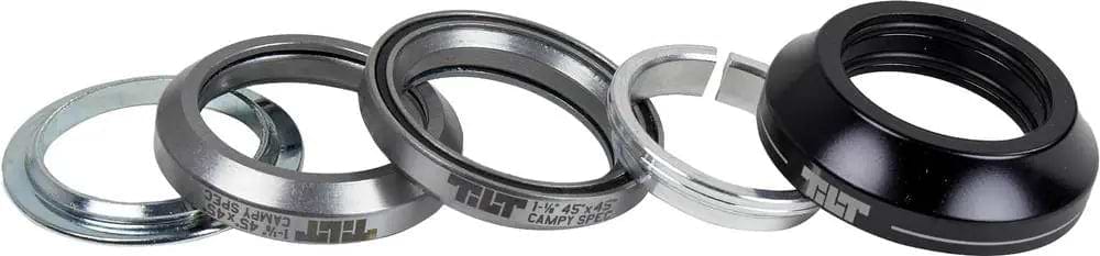 Five components of the Tilt Tall Stack Integrated Stunt Scooter Headset by Tilt—including two silver bearing cups with sealed bearings, a silver washer, a thin silver ring, and a black top cap—are displayed in a row on a white background.