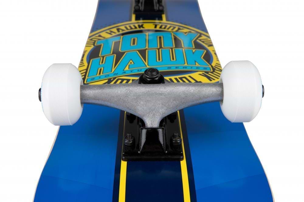 Close-up of the Tony Hawk SS 180+ Badge Logo Blue/Yellow Complete Skateboard (7.5" x 31") featuring bold yellow branding, white wheels, and a metal truck—an ideal Tony Hawk skateboard for beginners.