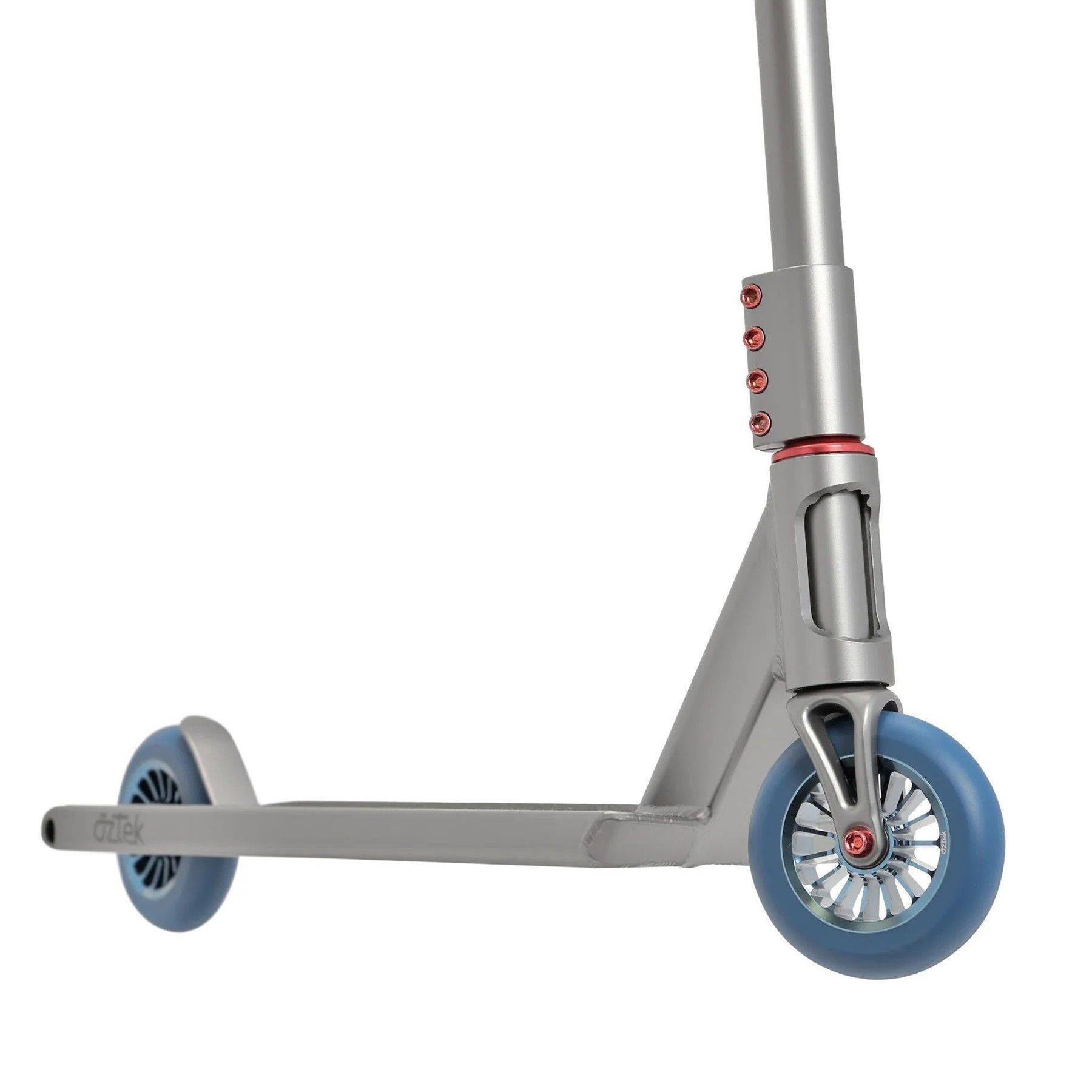 A close-up of the Aztek Siren Complete Street Stunt Scooter in grey, featuring blue wheels, red accents, and showing the deck, rear wheel, and part of the handlebar stem.