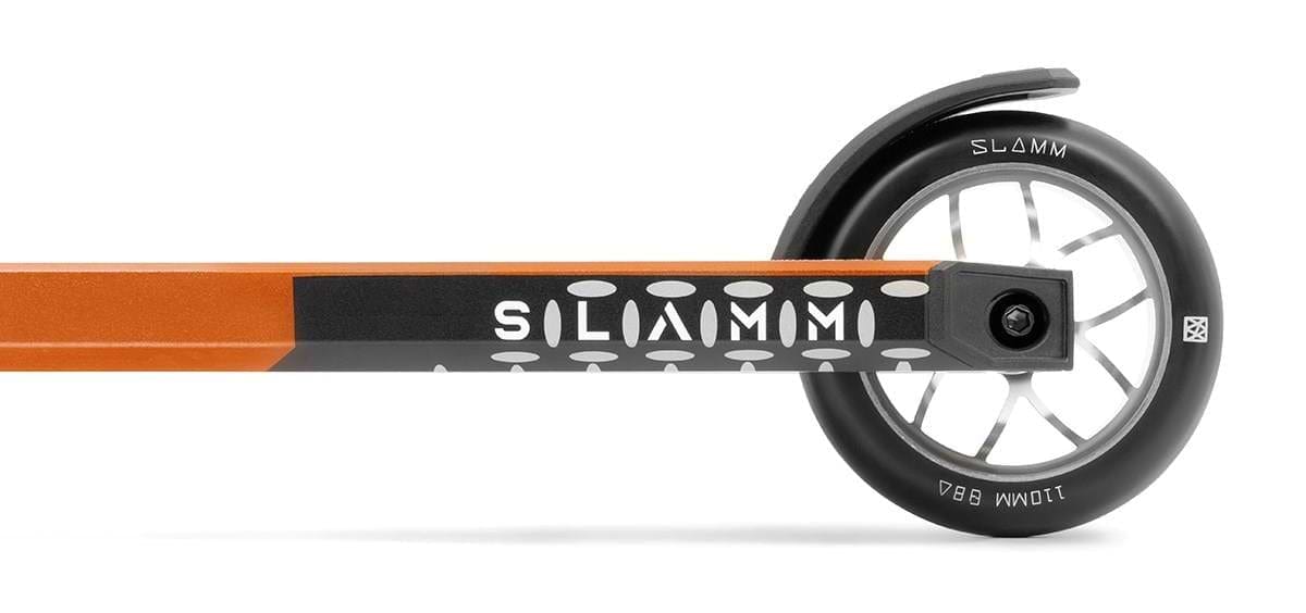 Close-up of a Slamm Assault Complete Stunt Scooter in orange, highlighting the 110mm black aluminum wheel with a white interior and metallic spokes. Perfect for skill improvement, the deck's side features a dotted pattern and the Slamm brand name.