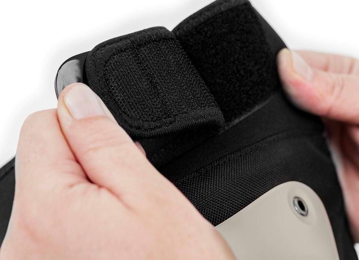 Close-up of two hands securing a black Velcro strap on fabric, part of the REKD Shield Triple Skate Protection Pad Set - Black / Beige by REKD for advanced action sports protection.