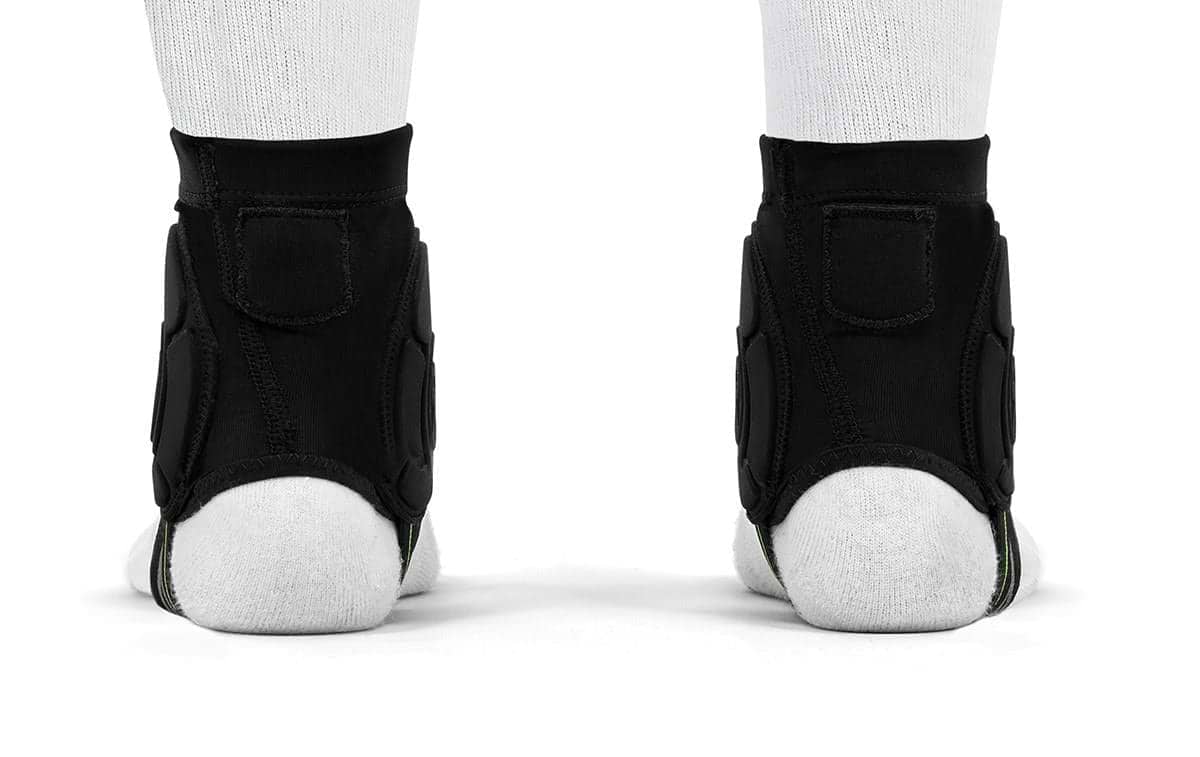 A rear view of two feet wearing white socks and REKD Energy Covert Ankle Impact Skate Protection Guards - Black by REKD, featuring energy-absorbing protection, standing side by side on a white surface.