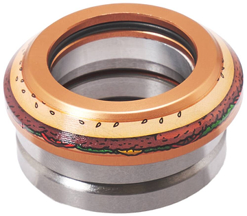 The image shows a detailed view of a metallic object that resembles the Chubby Integrated Stunt Scooter Headset - Burger Boy. It features a colorful design akin to a hamburger with buns, lettuce, tomato, and beef patty. The sealed bearing in the photo could seamlessly be part of a stunt scooter headset. The background is white.