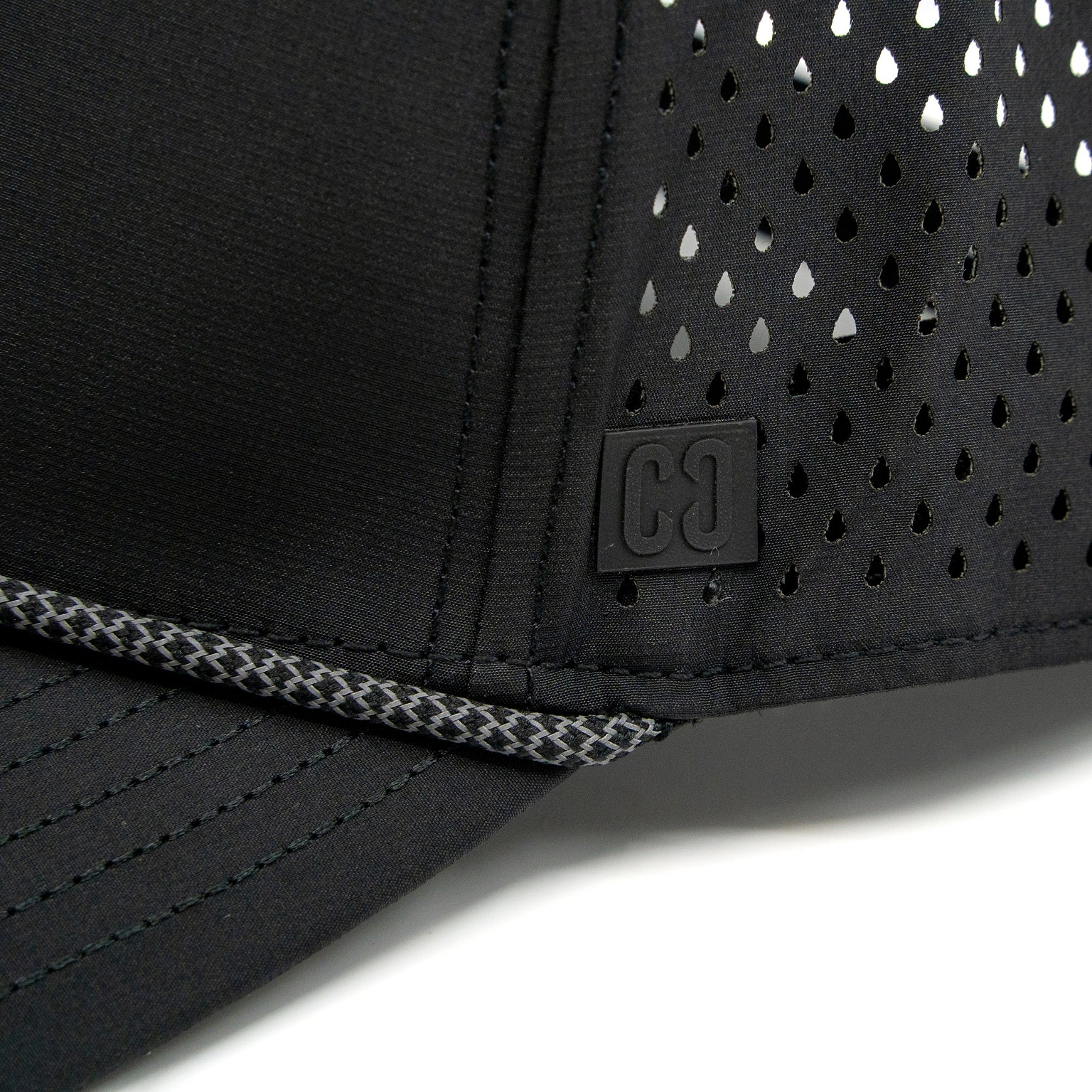 Close-up of the CORE Aero Rope Cap in black, featuring ventilated holes, prominent stitching, and a small square CORE logo patch with “C C” on the front near the brim.