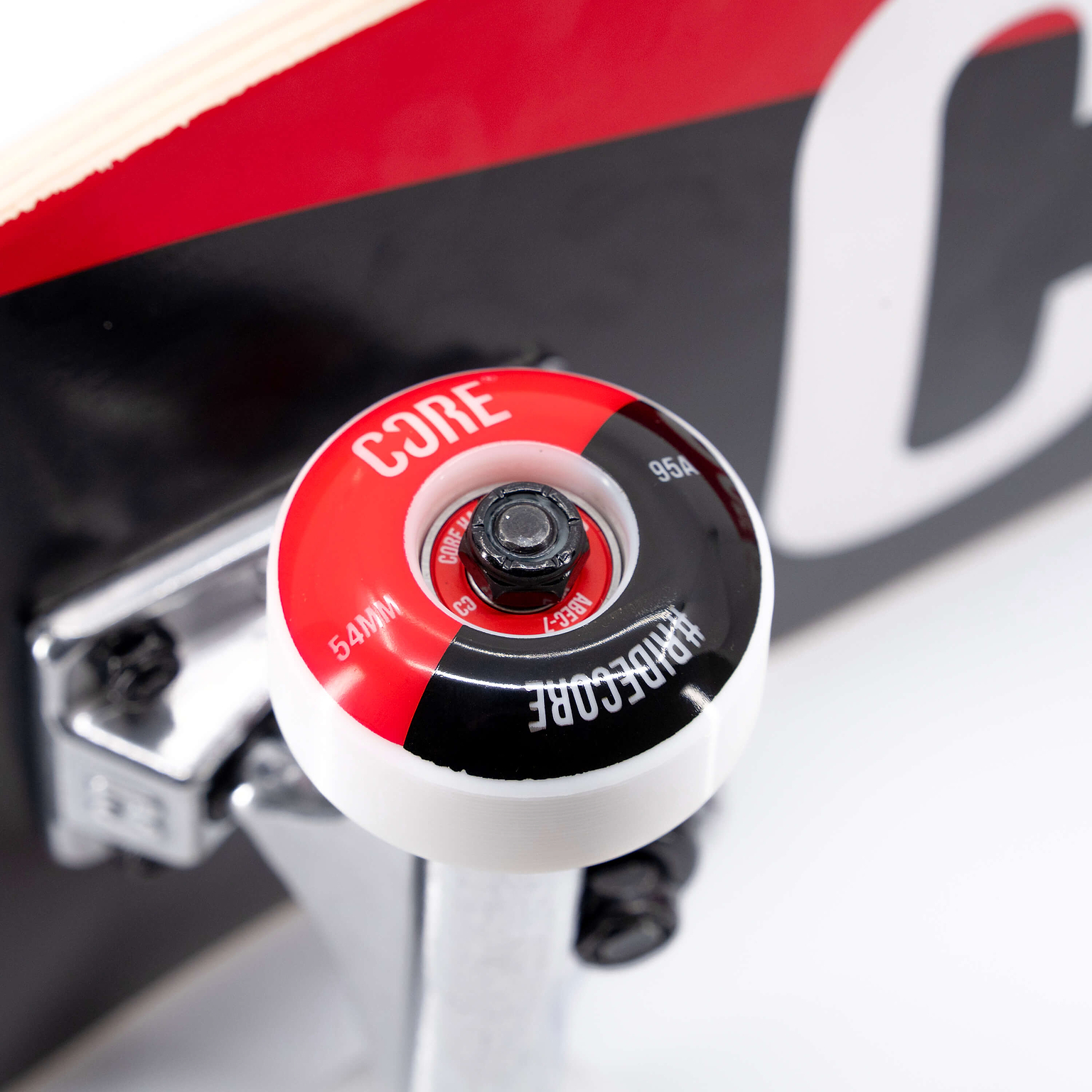 Close-up of a red, black, and white wheel on a silver truck mounted to a maple deck, featured on a CORE C2 Red / Black Split Complete Skateboard - 7.75″ x 31″.