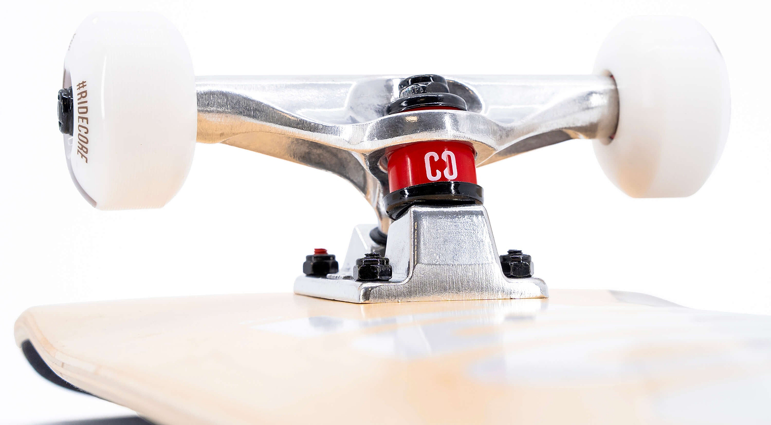 Close-up of a CORE C2 Red / Black Split Complete Skateboard - 7.75″ x 31″ truck with a red bushing attached to a light maple deck and white wheels.