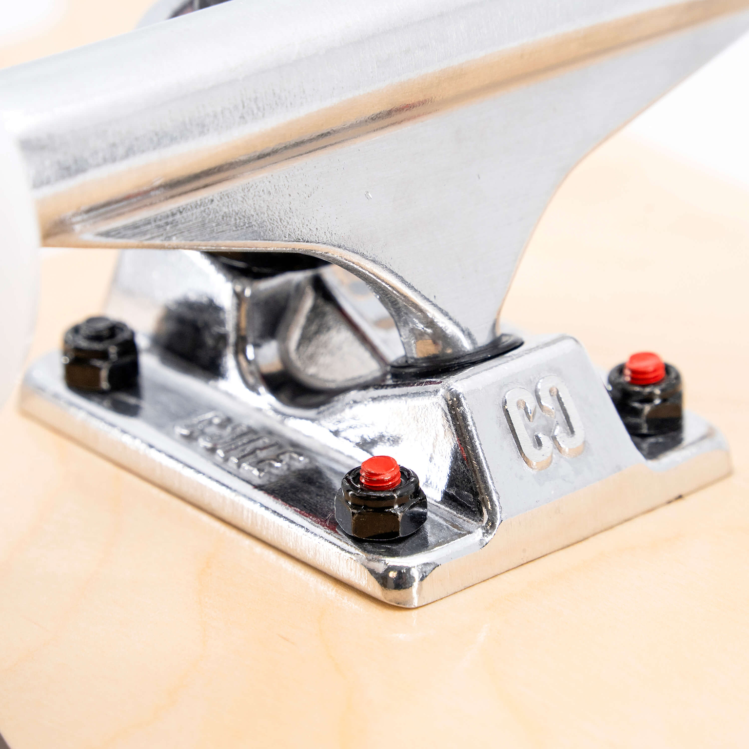 Close-up of a silver skateboard truck on a light-colored maple deck, featuring black hardware and red nuts on a CORE C2 Red / Black Split Complete Skateboard - 7.75″ x 31″.