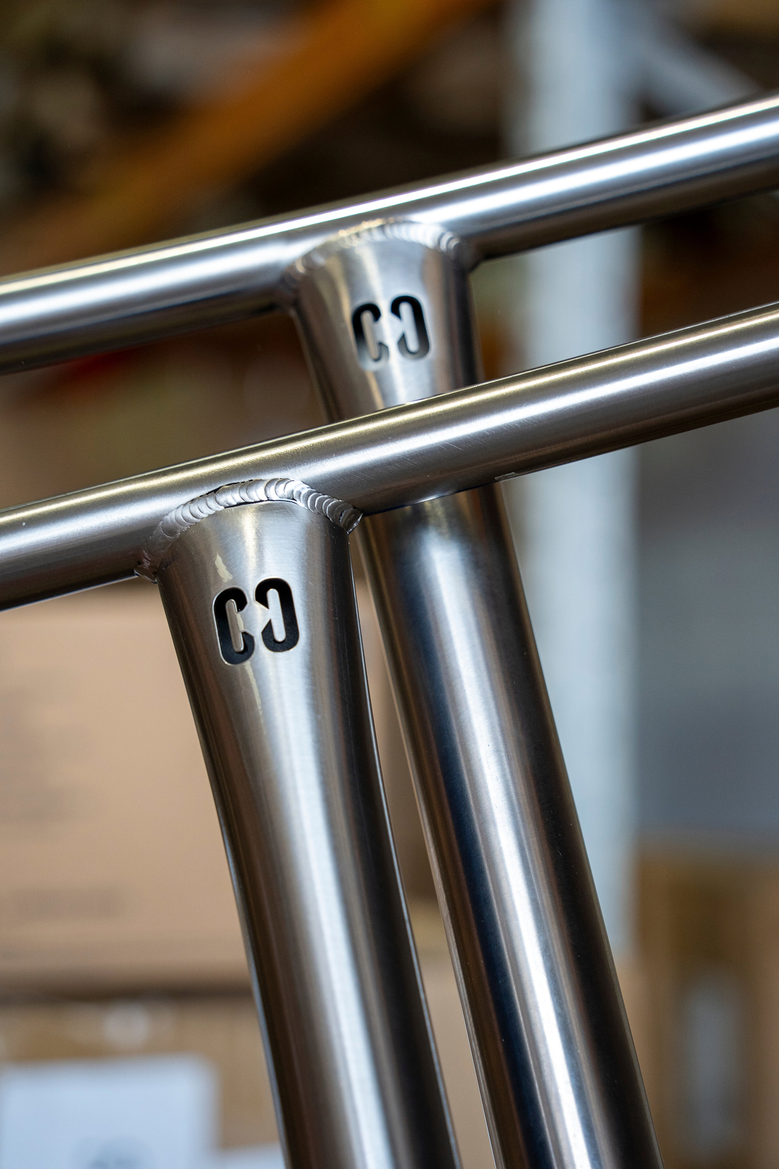 Close-up of CORE Halfbarz V2 Titanium Oversized HIC Stunt Scooter T-Bars, featuring a cut-out logo on the vertical tubes and visible metal welds at the joints.