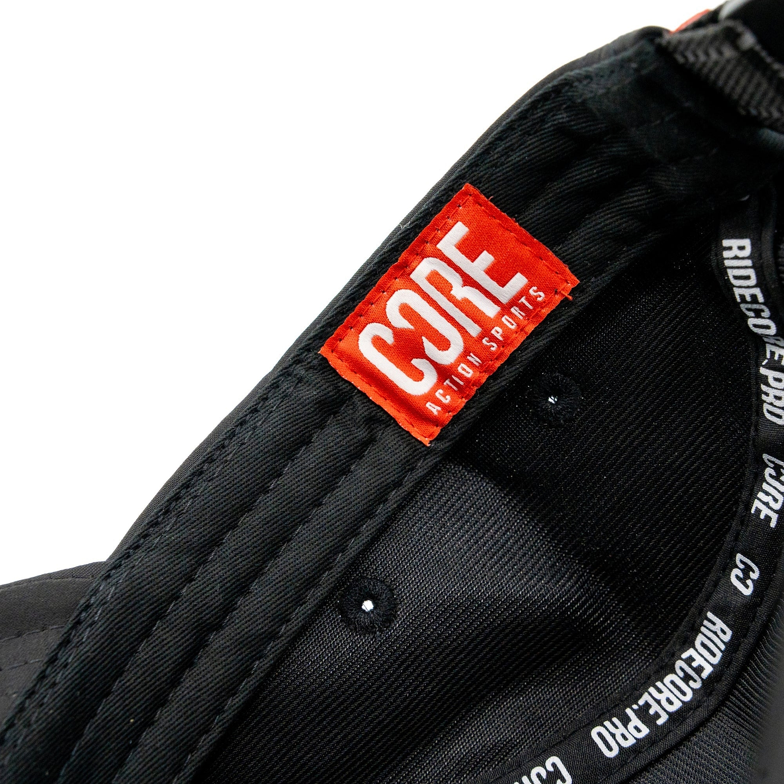 Close-up of the inside of the CORE Performance Cap – Black / Reflective, showing a red and white “CORE ACTION SPORTS” label and white text on the black inner band.