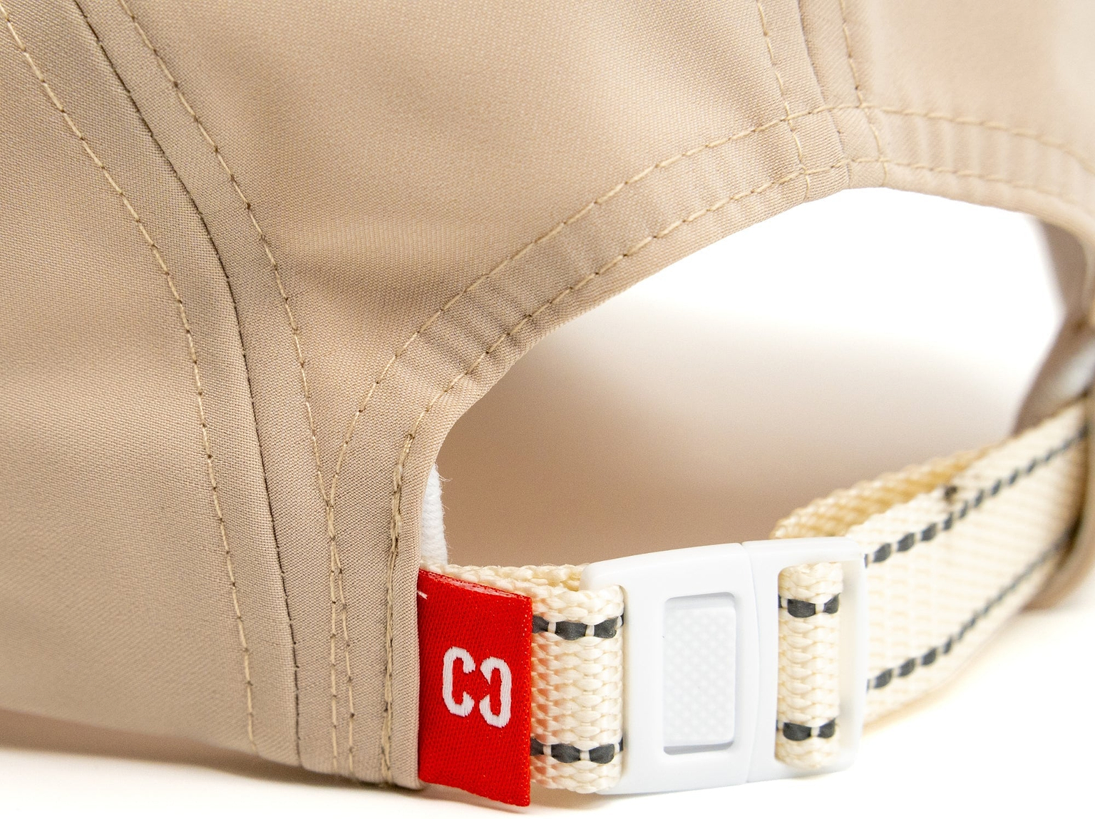 Close-up of the back of the CORE Performance Cap - Sand / Reflective, featuring a fabric strap with a plastic buckle and a small red tag displaying the number “33” in white. Crafted by CORE from breathable fabric for comfort during activity.