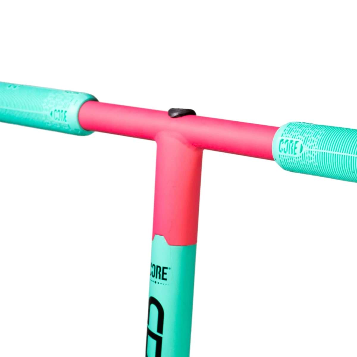 Close-up of the eco-friendly handlebar on the CORE CD1 Complete Stunt Scooter - Teal / Pink. The vibrant T-shaped bar is pink with bright turquoise grips, making it perfect for beginner riders. "CORE" is emblazoned on the grips, and the striking colors stand out against the white background.