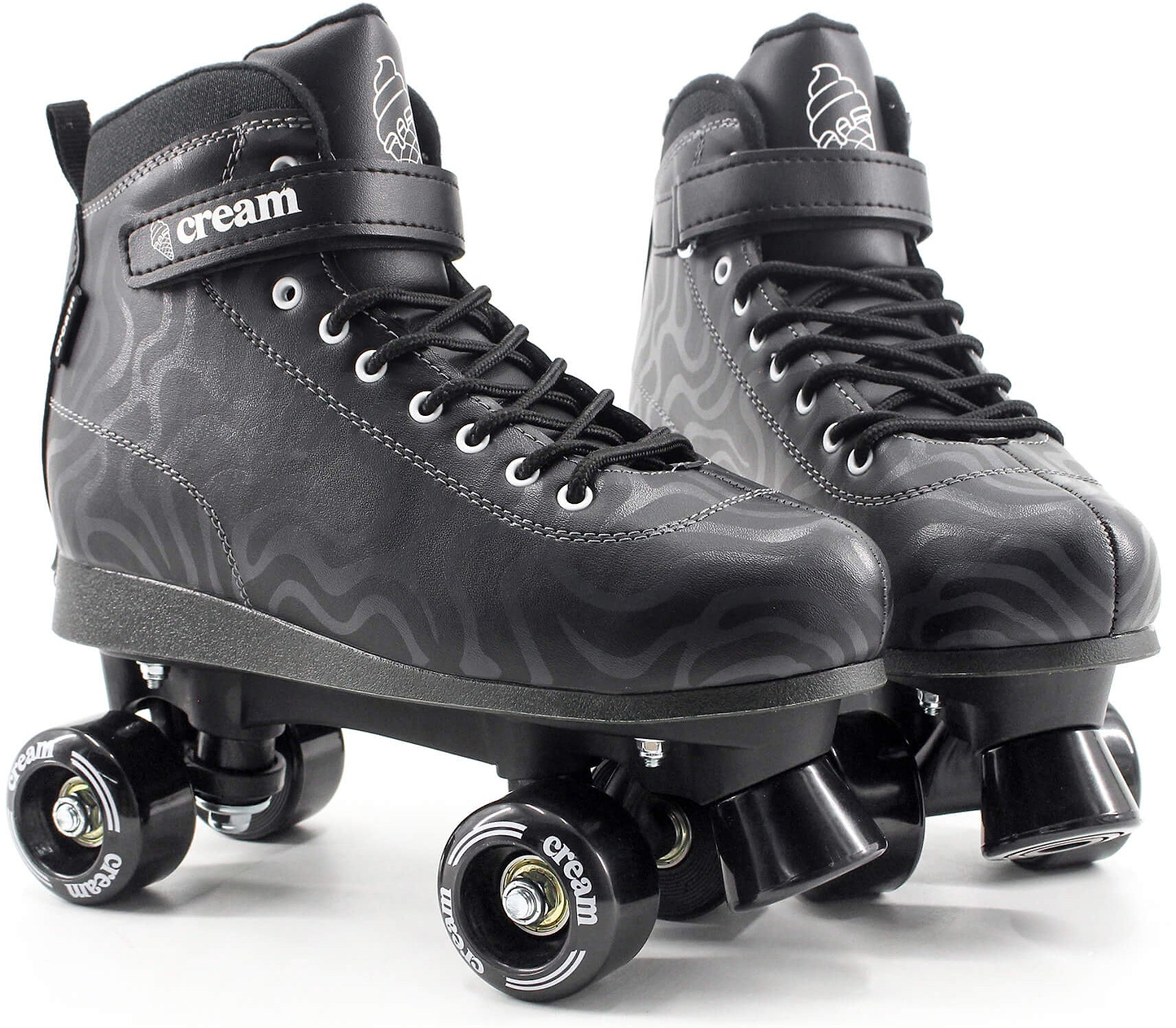 A pair of CREAM Scoop Wave Adjustable Quad Roller Skates in black, crafted from vegan leather and featuring laces, ankle straps, and four wheels each. These adjustable quad skates showcase subtle wavy patterns along with “CREAM” branding on the strap and wheels.