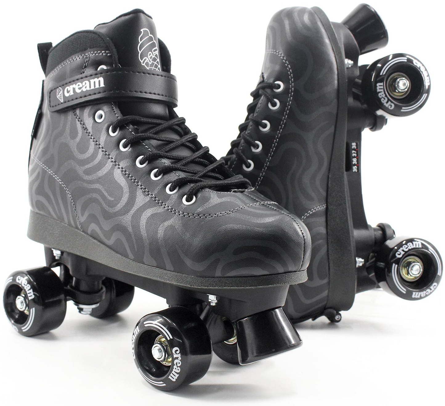 A pair of CREAM Scoop Wave Adjustable Quad Roller Skates in black, featuring vegan leather construction with a wavy gray pattern, black laces, and “CREAM” branding on the strap and wheels. Perfect for beginners, one skate is displayed upright while the other rests on its side to showcase the wheels.
