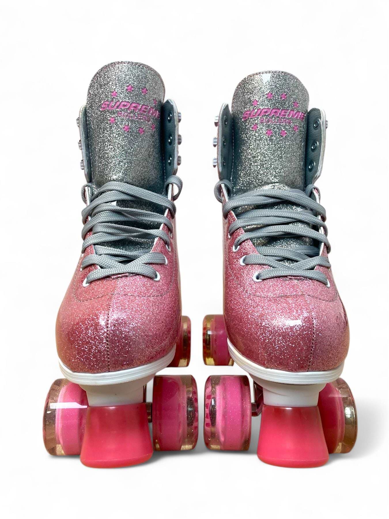 The Supreme Del Rey Adjustable Quad Roller Skates in pink by Supreme feature glittery pink and silver design, gray laces, and pink wheels, shown from the front against a white background.