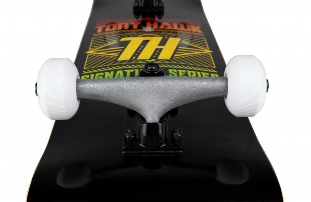 Close-up of the Tony Hawk SS 180+ Stacked Logo Black Complete Skateboard (8" x 31.5") featuring white wheels, silver trucks, and a black deck with the yellow and orange stacked logo graphic, focused on the front wheel and truck.