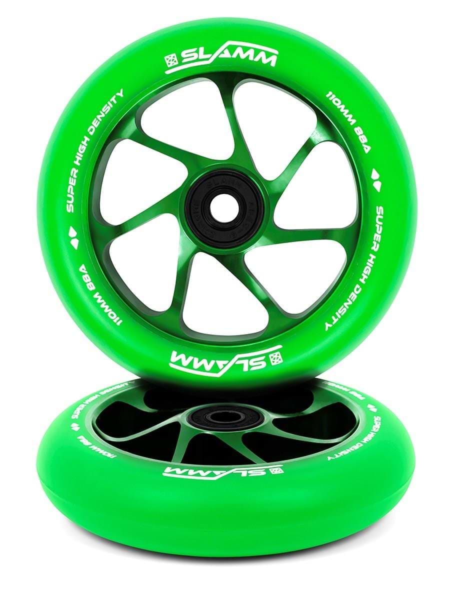 Two green Slamm Team 110mm stunt scooter wheels, featuring aluminium cores with black spokes and hubs. Both have high-rebound PU and white SLAMM branding—one stands upright, the other lies flat below.