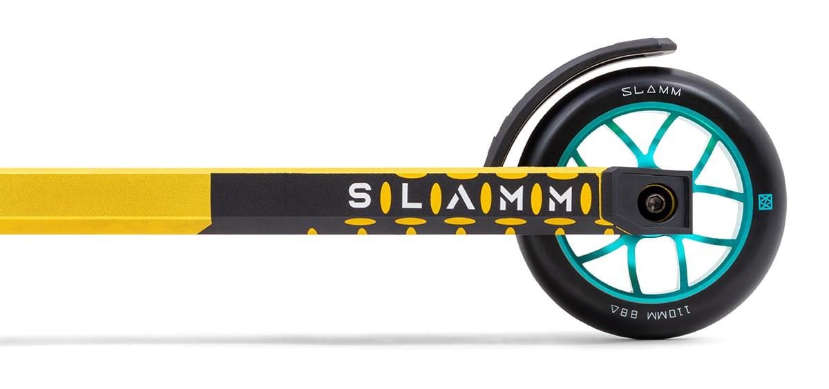 Close-up image of the rear wheel of a gold Slamm Assault Complete Stunt Scooter. The scooter features a teal and black 110mm aluminum wheel, with "SLAMM" printed on the frame and fender. The tire is marked "88A," enhancing its sleek alloy deck design.