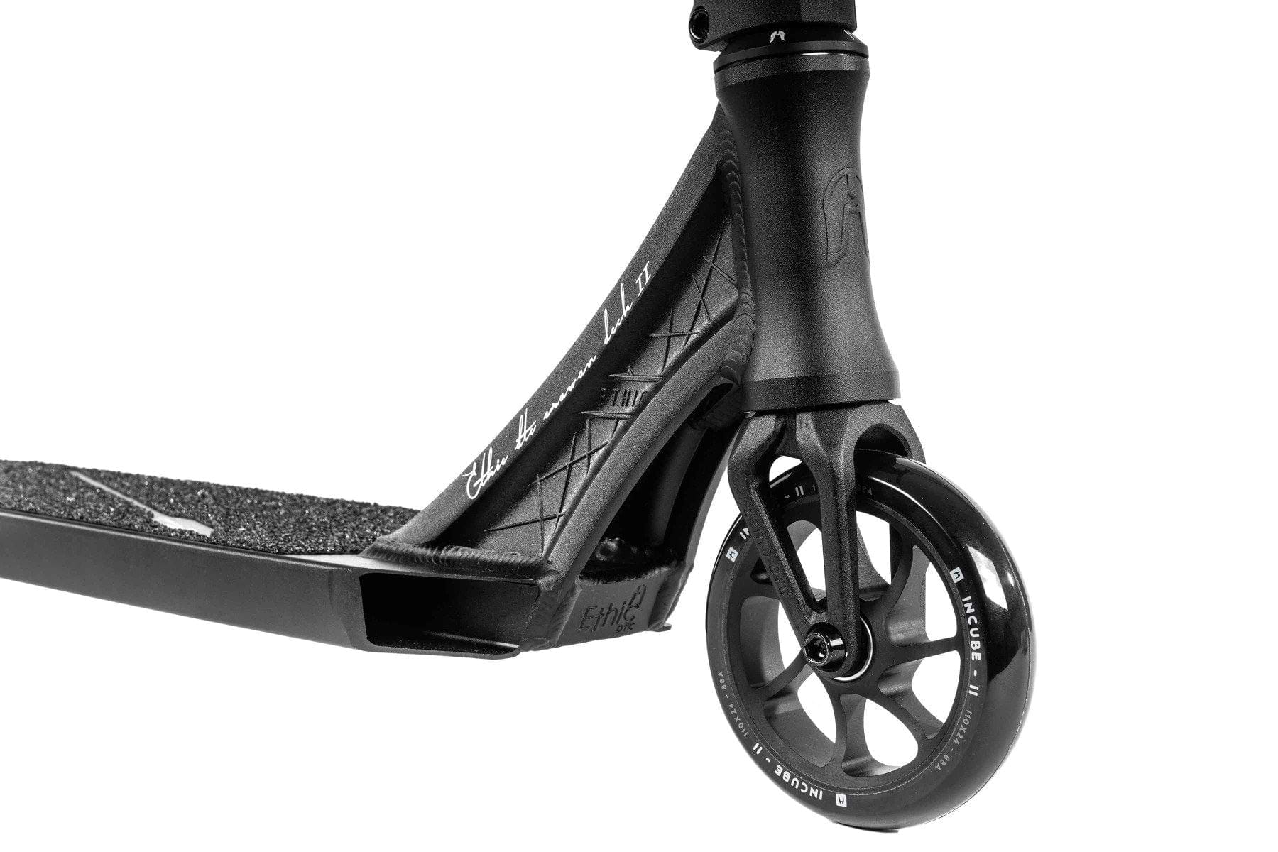 Close-up of the front wheel and deck of the Ethic DTC Erawan V2 Complete Stunt Scooter (S) - Black, featuring a sleek design. The silver-accented wheel is attached to an angular deck with grip tape, making it one of the lightest scooters available. Subtle Ethic branding enhances its appeal, highlighting both durability and style for this complete stunt scooter.
