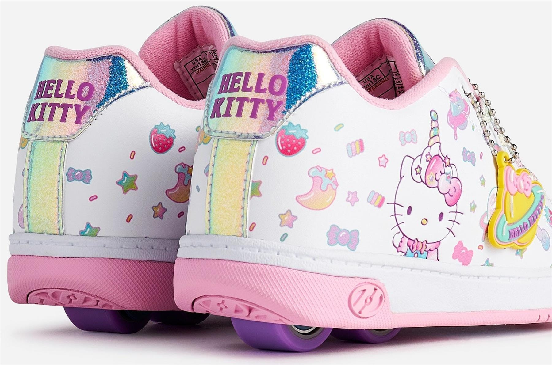 The Heelys x Hello Kitty Split X2 Girls Heelys in white and pink feature Hello Kitty graphics, rainbows, strawberries, stars, pastel patterns, "HELLO KITTY" text on the heel, and pink wheels. Brand: Heelys.