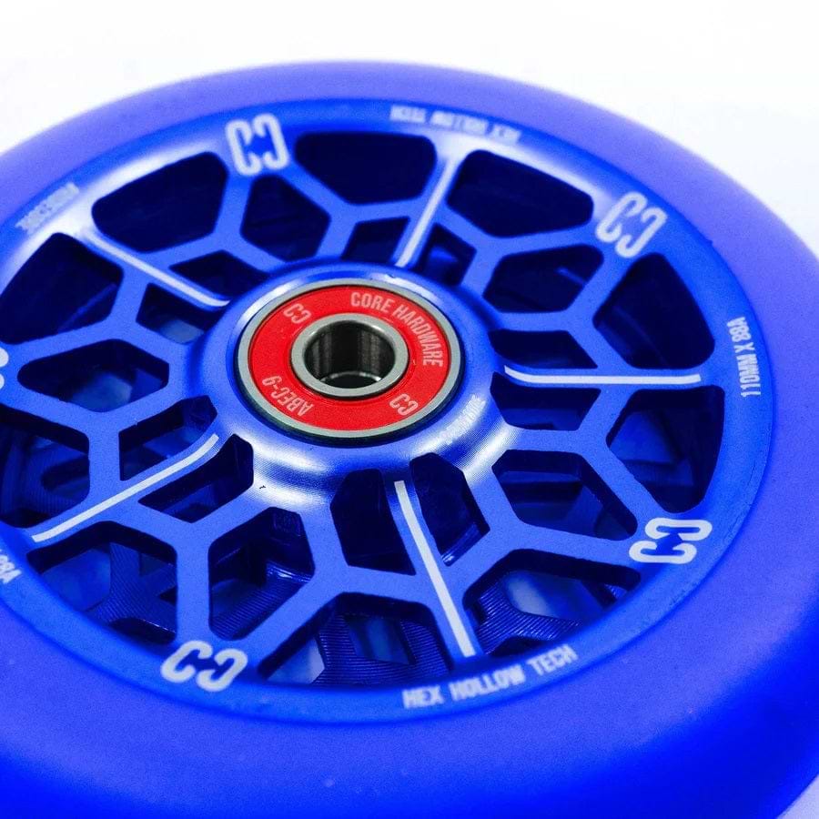 A close-up of the CORE Hex Hollow Core 110mm Stunt Scooter Wheel in navy blue showcases a hexagonal spoke pattern and a red core bearing the "CORE" brand. Featuring HEX Hollow Tech design, the wheel includes text on its rim and boasts an ABEC 9 bearing at its center for enhanced smooth performance.