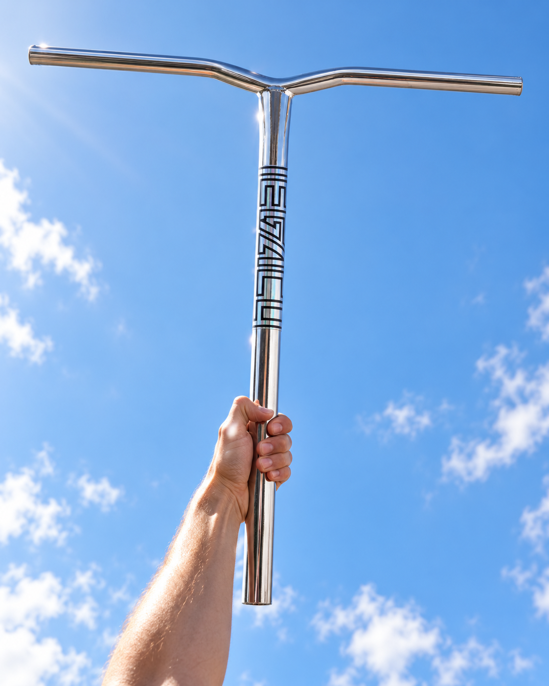 A hand holds polished chrome Legacy Ventus Steel Standard IHC Stunt Scooter Bars in a T-shape against a bright blue sky.