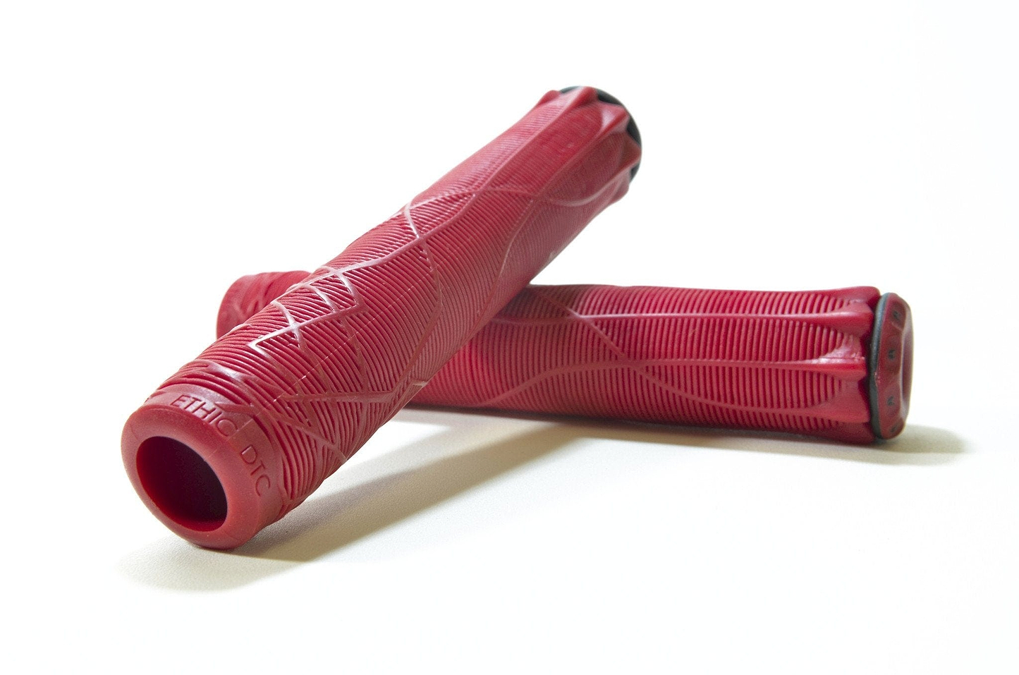 A pair of Ethic DTC Red Stunt Scooter Grips - 170mm, featuring textured patterns, rests on a white surface. Crafted from thermoplastic rubber, these cylindrical grips display intricate grooves and lines for improved grip, making them an ideal blend of style and functionality for your ride.