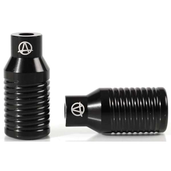 Two Apex Bowie Aluminium Stunt Scooter Pegs in black are displayed, featuring a cylindrical and ribbed design. One peg is placed upright while the other is laid on its side. Both showcase the Apex logo, a stylized "A" within a circle, indicative of their high-quality craftsmanship.