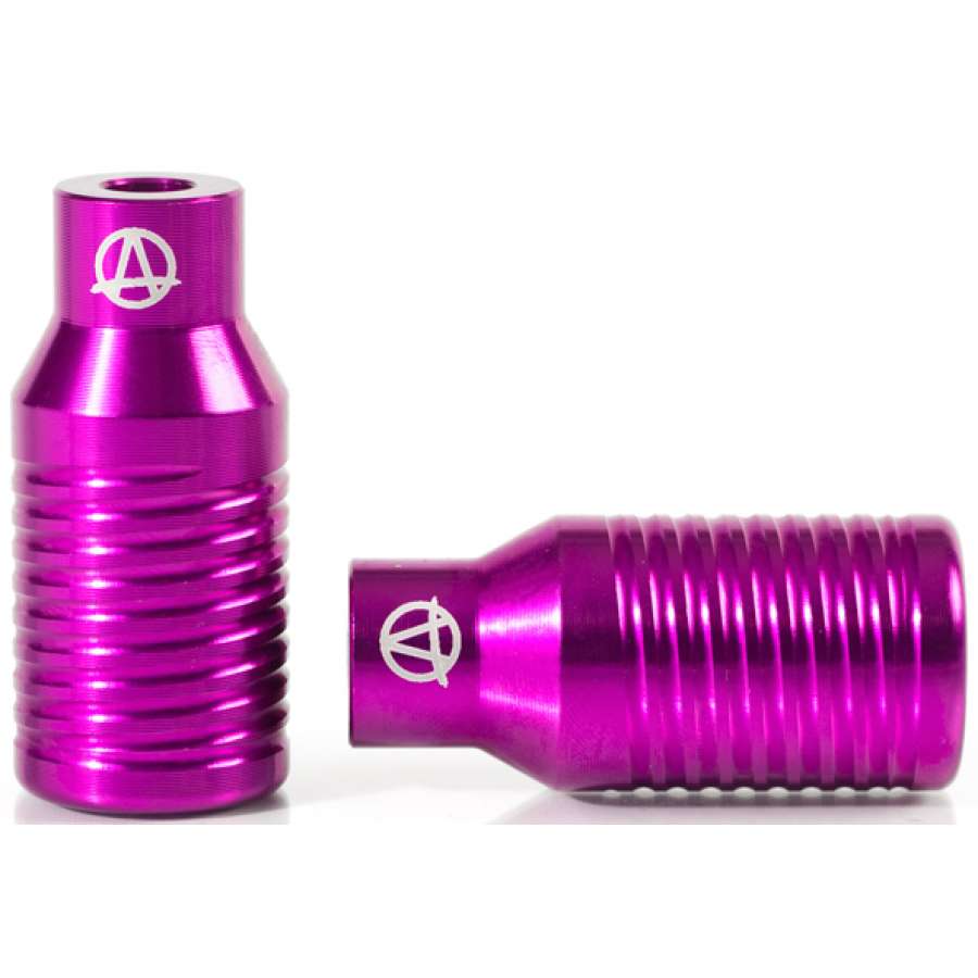 Displayed are two sleek Apex Bowie Aluminium Stunt Scooter Pegs in metallic purple. One stands upright, while the other rests horizontally. These lightweight aluminium pegs feature a ridged texture and display a circular emblem with an "A" at the center.