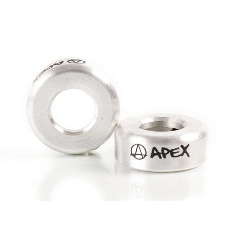 Two raw silver, circular metal BMX headset spacers with a hole in the center display the word "APEX" alongside an anarchy symbol in black. One spacer stands upright while the other rests on its side against a white background, enhancing your scooter accessories collection similarly to the Apex Aluminium Scooter Bar Ends - Raw Silver.
