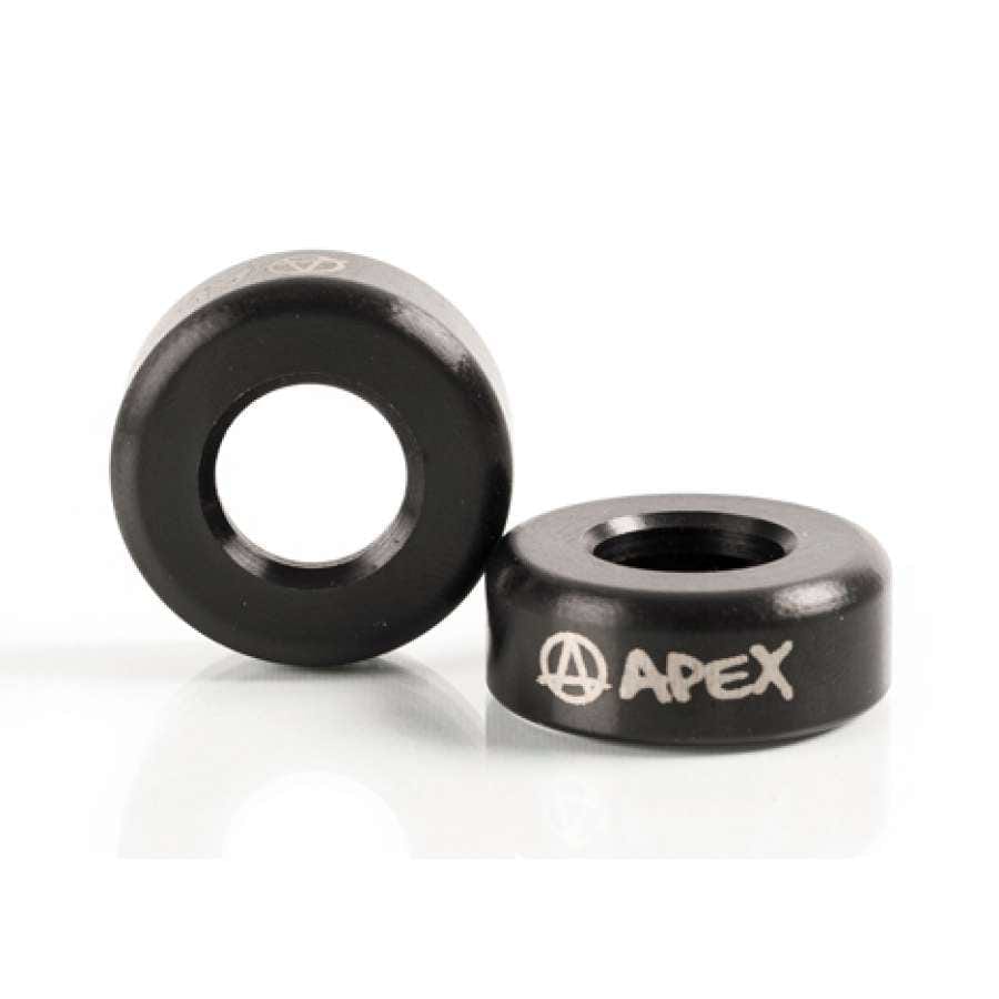Two black metal washers, one standing upright and the other lying flat, resemble the sleek design of Apex Aluminium Scooter Bar Ends - Black. Both feature the brand name "APEX" and a stylized letter "A" inscribed on their surface. The clean white background accentuates their design from Apex.