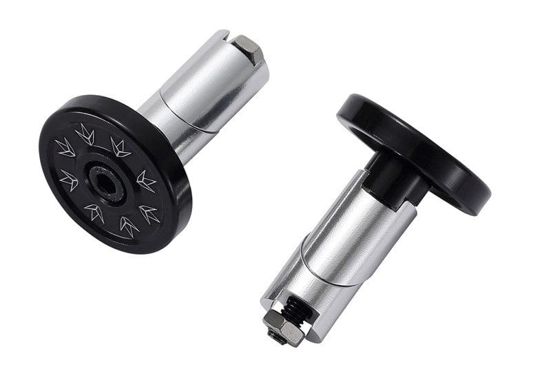 The Blunt Envy Alloy Scooter Bar Ends in black feature a pair of metallic, cylindrical ends with circular caps that display arrow designs. Designed for durability from a robust alloy and featuring an expandable structure, these bar ends ensure compatibility with various setups. They are showcased on a white background, artistically positioned at different angles.