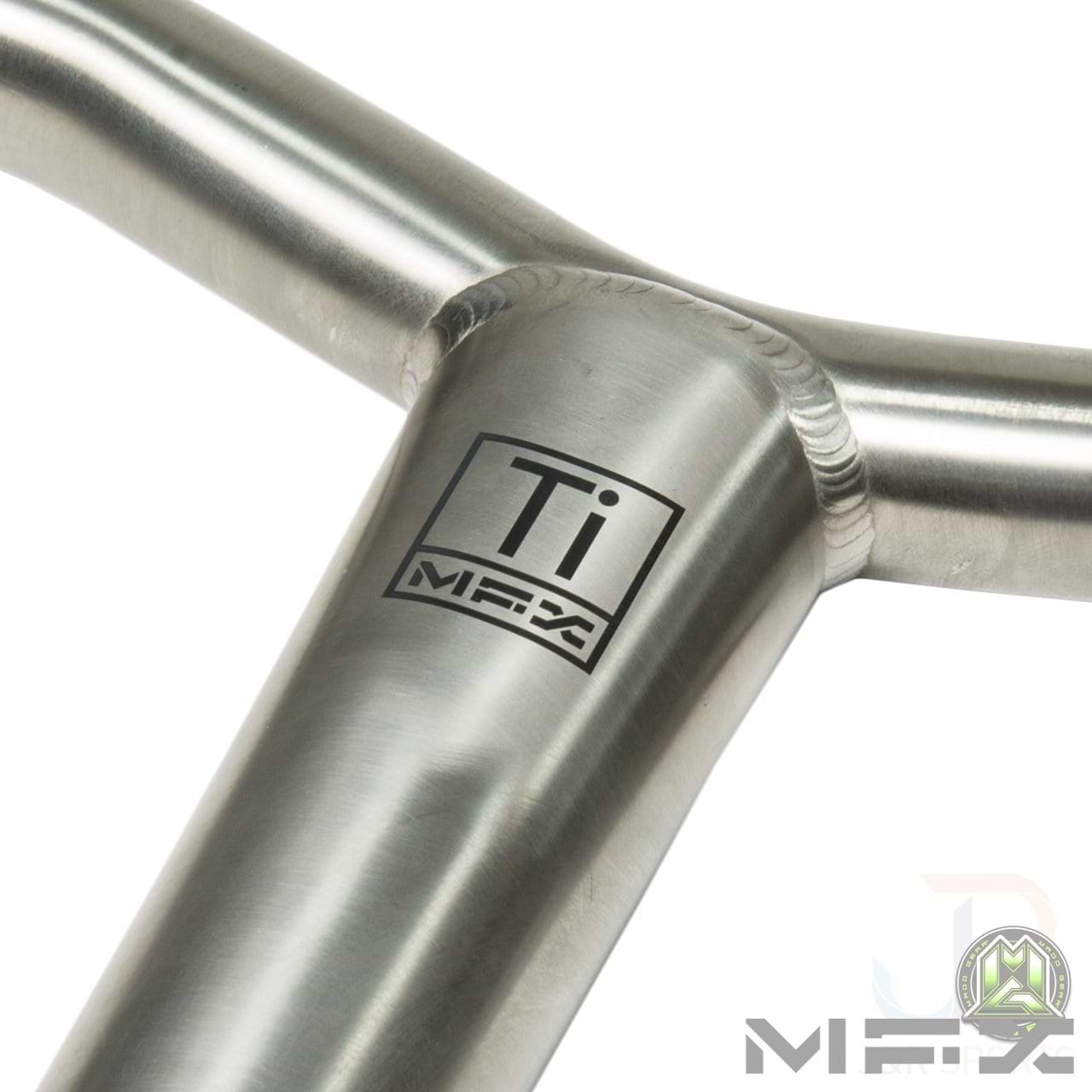 Close-up of a metal T-joint with a smooth weld, featuring the logo "Ti MFX" printed on the surface. Crafted from Grade 9 Titanium, this piece showcases exceptional craftsmanship and robust design, similar to the Madd Gear MGP MFX BAMF Titanium Oversized SCS Stunt Scooter Bar - Raw 660mm x 660mm. The plain background accentuates its shiny, metallic texture.