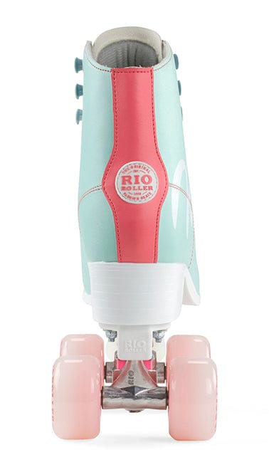 The image features the Rio Roller Script Quad Roller Skate, adorned with four pink wheels. The boot is crafted from mint green PVC leather, accented by a coral pink stripe down the back, and displays the "Rio Roller" logo. The skate is displayed from behind against a white background.