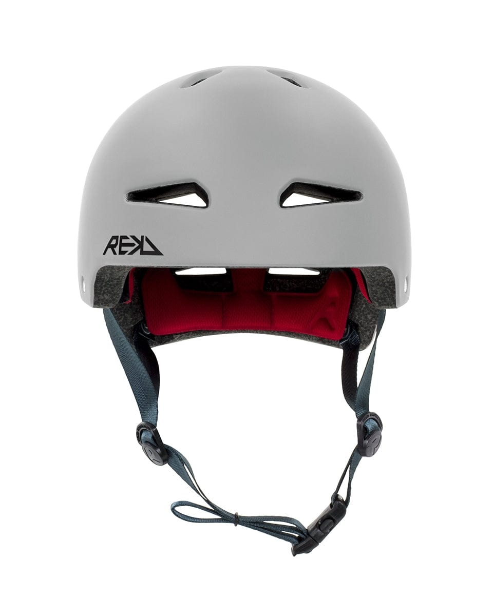 The REKD Ultralite In-Mold Skate / Scooter Helmet in grey showcases a design with ventilation slits, a black adjustable chin strap, and red interior padding. Enhanced by In-Mold technology, it's ideal for safe cycling or skateboarding adventures. The REKD brand logo is prominently displayed on the side.