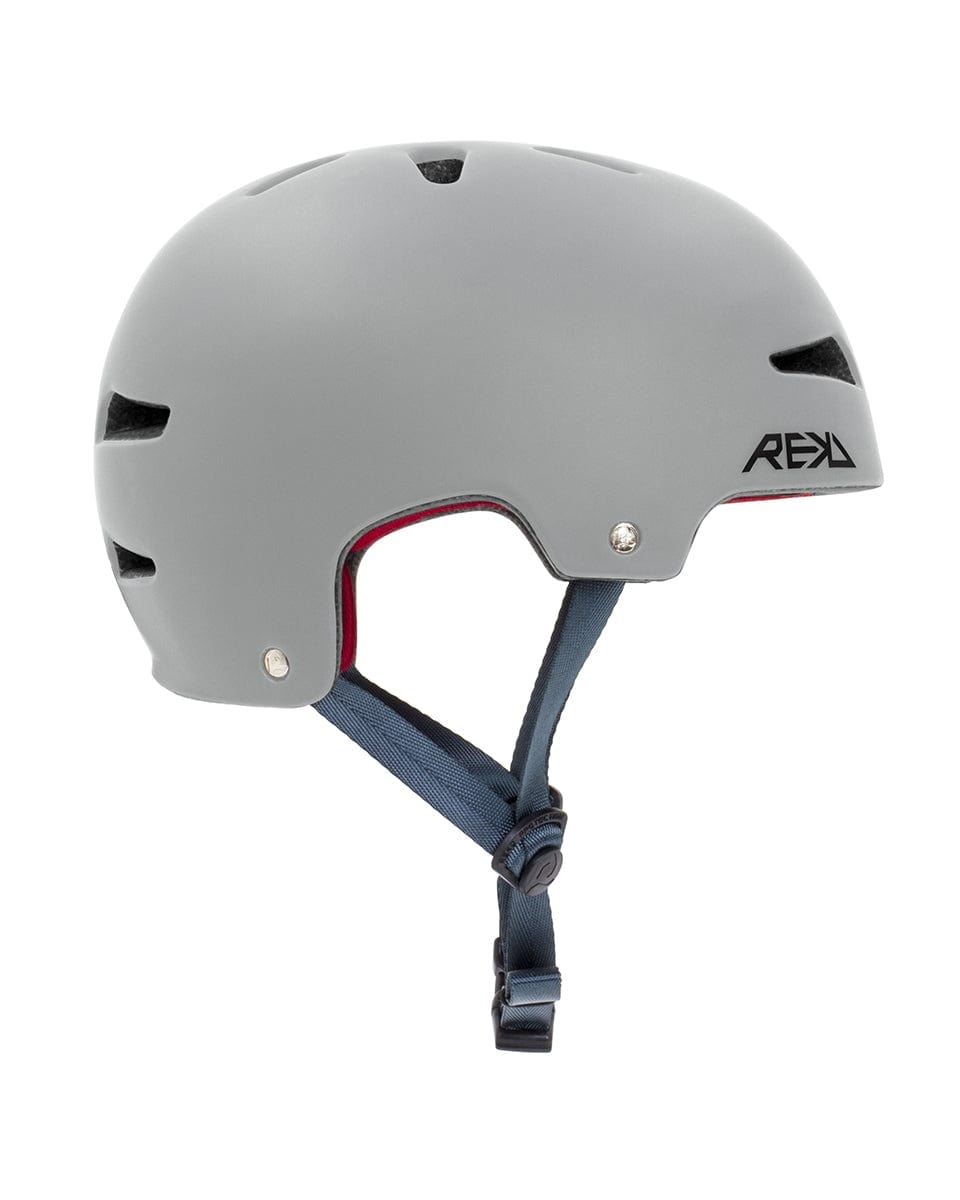 The REKD Ultralite In-Mold Skate/Scooter Helmet in gray features ventilation slits on the top and sides, with a black logo on the left side. Designed for action sports, it incorporates In-Mold technology and has an adjustable blue chin strap with a black buckle. The interior lining stands out in vibrant red.