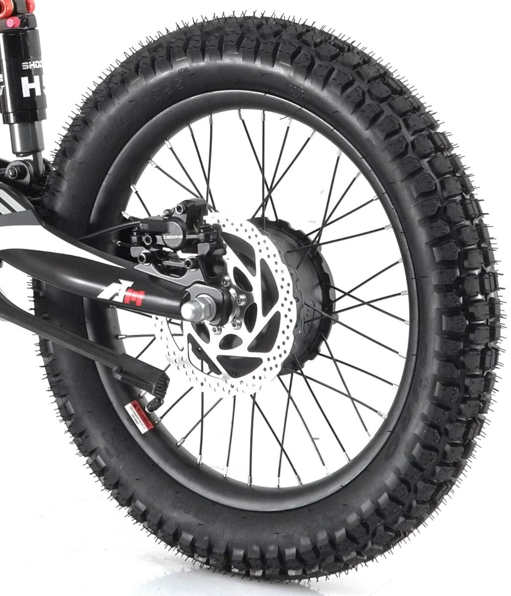 Close-up of a black bicycle wheel featuring thick, knobby tires and hydraulic disc brakes. The spokes are black, and the bike's frame is partially visible with a suspension fork, closely resembling the robust design found in the Revvi 18" Kids Electric Balance Bike - Green.