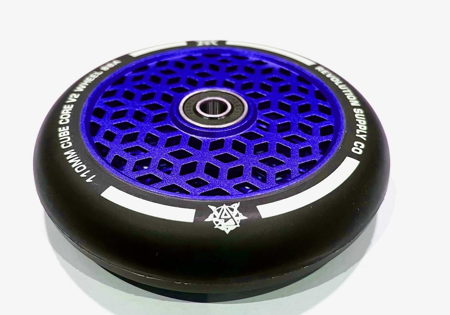 The Revolution Cubed Core Ultralite 110mm Stunt Scooter Wheel in Blue features a striking black and blue design that highlights its innovative Cubed Core Ultralite technology. The wheel showcases a geometric pattern accented by white text along the edge, while its honeycomb core integrates cube core cutouts and a visible central bearing, adding to its sleek appearance.