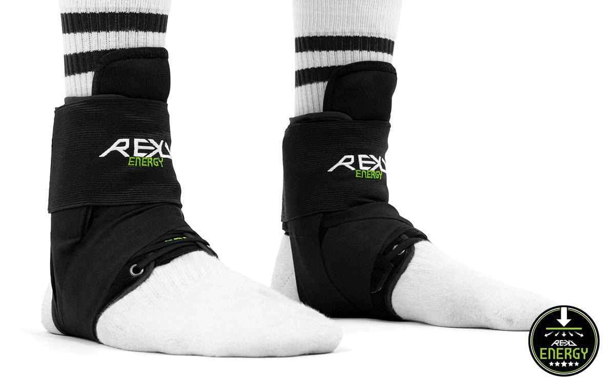 A person is wearing REKD Energy Covert Ankle Skate Protection Braces in black over white socks with black stripes. These supports, branded under "REKD," ensure maximum ankle protection. The logo in the bottom right corner proudly displays the bold REKD branding, reaffirming their commitment to quality and support.