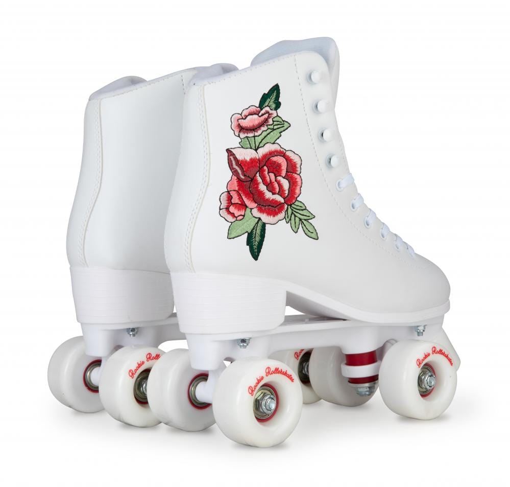 The Rookie Rosa Quad Roller Skates in white by Rookie feature embroidered red roses on the sides. These vegan-friendly skates are highlighted with elegant white laces and vivid red accents on the wheels, set against a plain white background.
