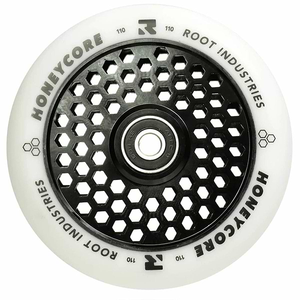 The Root Industries Honeycore 110mm Stunt Scooter Wheel in white and black boasts a distinctive honeycomb cut-out design on the core. It is equipped with premium Root bearings, and the brand's name is prominently displayed in bold along the outer edge for a sleek finish.