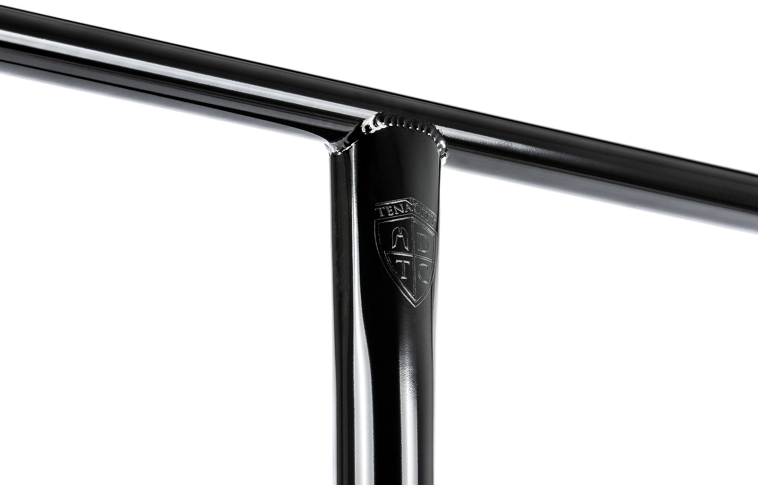 Close-up of a glossy black metal T-joint featuring a small engraved shield logo reading “TENN” on the vertical bar, showcasing the exceptional craftsmanship of the Ethic DTC Tenacity V2 Steel Oversized HIC Stunt Scooter T-Bars in Black Mirror (770mm x 600mm). Manufactured by Ethic, these oversized chromoly steel bars deliver outstanding strength and durability for demanding riders.