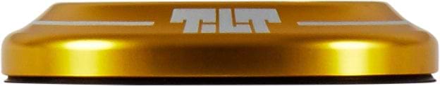 The Tilt Integrated Stunt Scooter Headset - Gold by Tilt is a gold, round item with a flat, circular top featuring the word "TILT" in white. The design incorporates two horizontal lines extending from the text and includes an anodized dust cover for a shiny, metallic look.