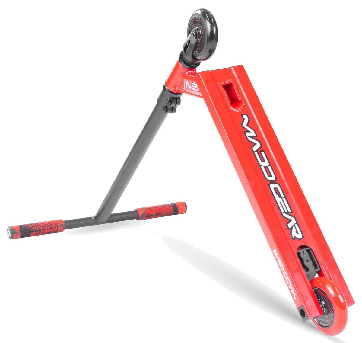 The Madd Gear (MGP) MG 1 Raven Complete Stunt Scooter in red/black is shown tilted, highlighting its deck, single front wheel, and handlebars with red and black grip tape. The Madd Gear logo appears on the deck.